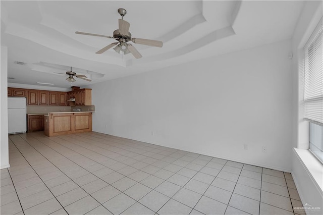 unfurnished living room featuring light tile patterned floors, a raised ceiling, ceiling fan, and a healthy amount of sunlight