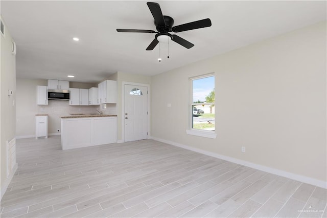 unfurnished living room featuring light hardwood / wood-style floors, ceiling fan, and sink