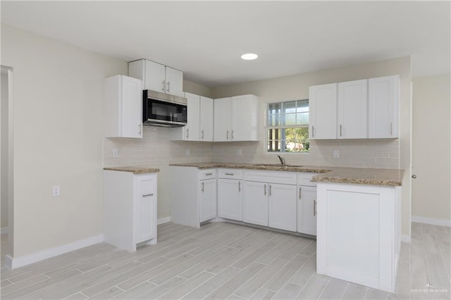 kitchen with light stone countertops, white cabinetry, sink, and tasteful backsplash