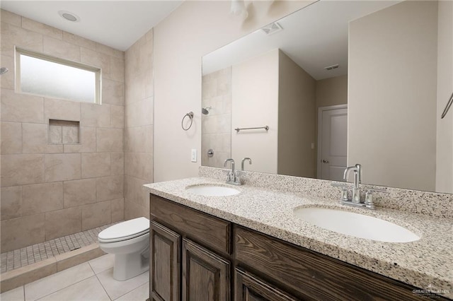 bathroom with tile patterned flooring, vanity, toilet, and tiled shower