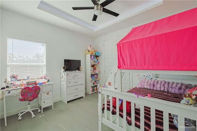 bedroom with a tray ceiling, wood finished floors, baseboards, and ceiling fan