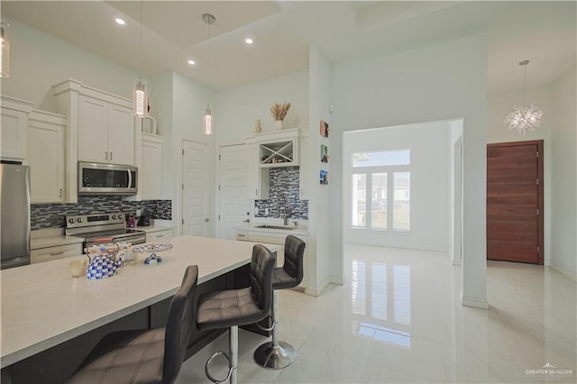 kitchen featuring a breakfast bar area, appliances with stainless steel finishes, a high ceiling, white cabinets, and a sink