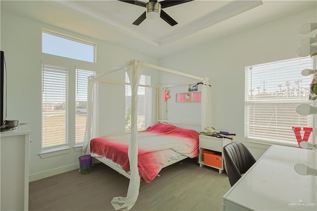 bedroom with a raised ceiling, wood finished floors, baseboards, and ceiling fan