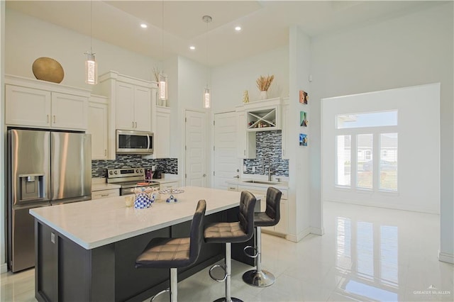 kitchen featuring a breakfast bar area, a kitchen island, white cabinets, a towering ceiling, and appliances with stainless steel finishes