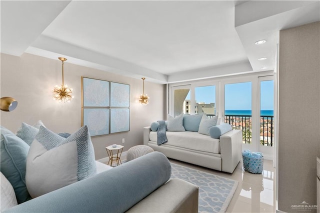 tiled living room featuring a raised ceiling, a water view, and a chandelier