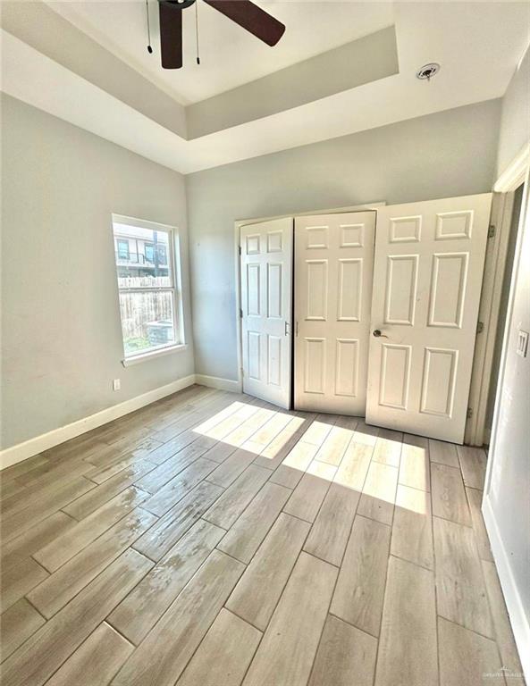 unfurnished bedroom featuring ceiling fan, a closet, a tray ceiling, and light hardwood / wood-style flooring