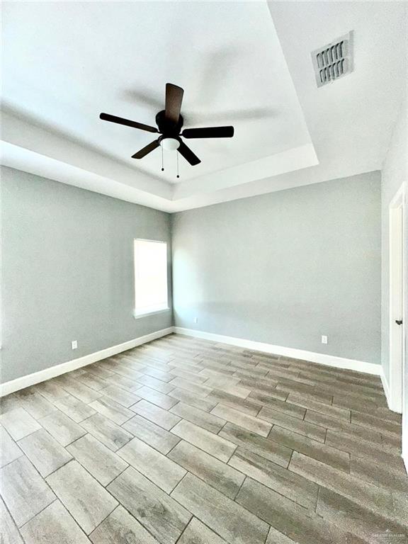 unfurnished room with ceiling fan, light hardwood / wood-style floors, and a tray ceiling