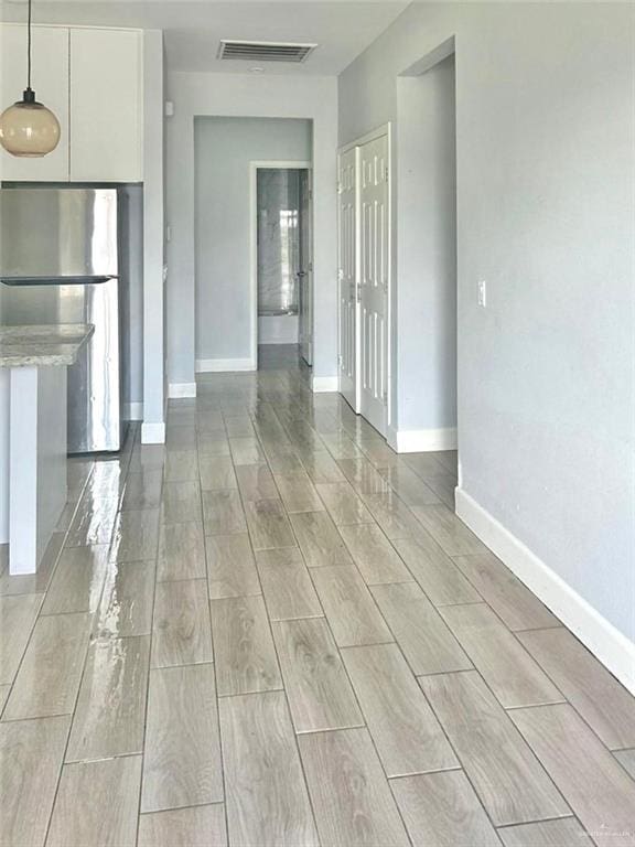 interior space featuring white cabinetry, light stone counters, light hardwood / wood-style flooring, stainless steel fridge, and decorative light fixtures