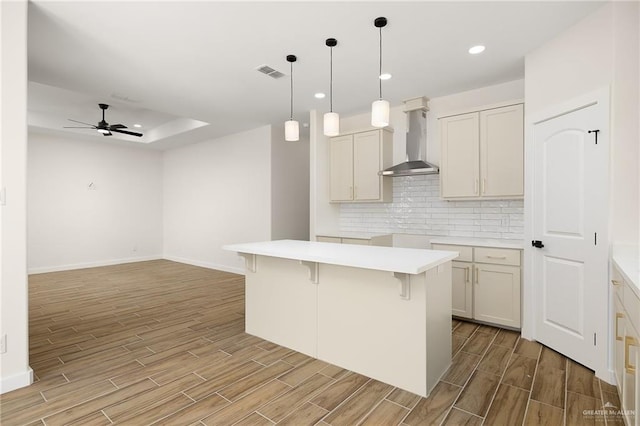 kitchen with a kitchen island, decorative backsplash, hanging light fixtures, ceiling fan, and wall chimney range hood