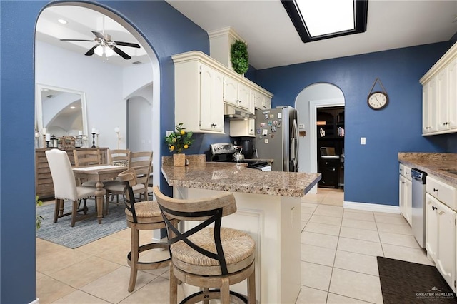 kitchen featuring stainless steel appliances, arched walkways, light tile patterned flooring, and a peninsula