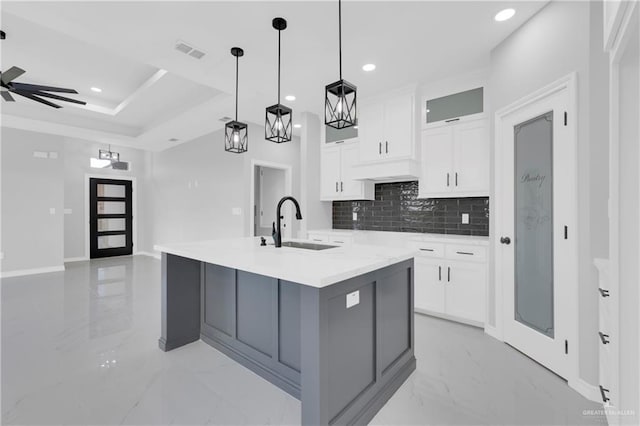 kitchen with a large island with sink, hanging light fixtures, decorative backsplash, ceiling fan, and white cabinetry