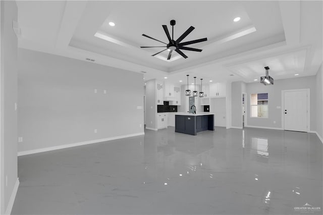 unfurnished living room with a raised ceiling, ceiling fan, and sink