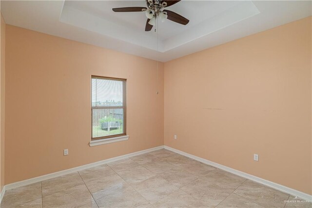 empty room with ceiling fan and a tray ceiling