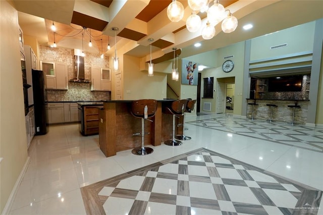 interior space featuring wall chimney range hood, tasteful backsplash, pendant lighting, a kitchen bar, and light tile patterned floors