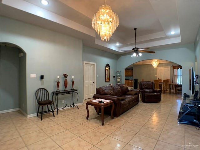 tiled living room featuring a raised ceiling and ceiling fan with notable chandelier