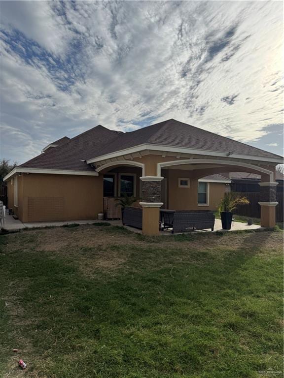 rear view of property featuring a lawn, fence, and stucco siding