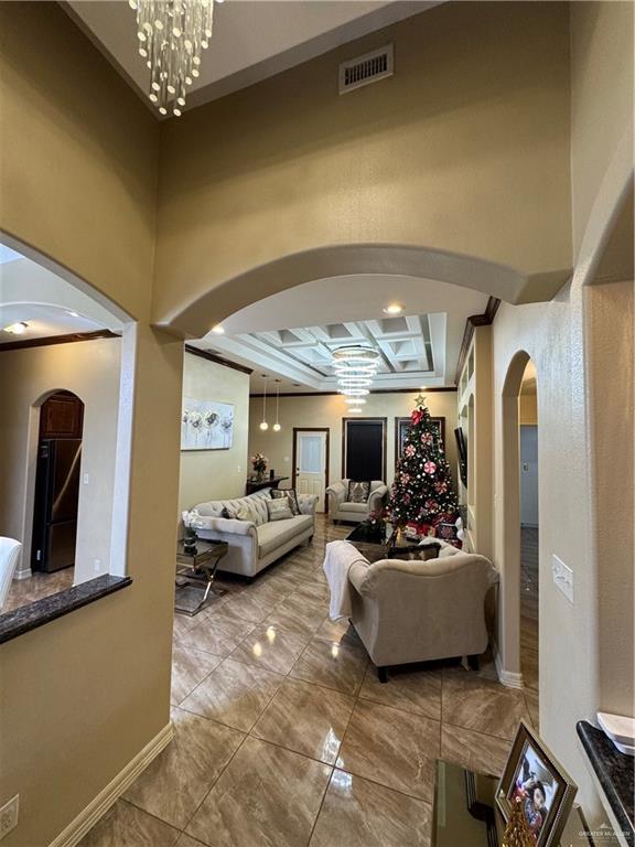 living area with arched walkways, a notable chandelier, coffered ceiling, visible vents, and baseboards