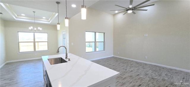 kitchen with sink, pendant lighting, a tray ceiling, a center island with sink, and light wood-type flooring