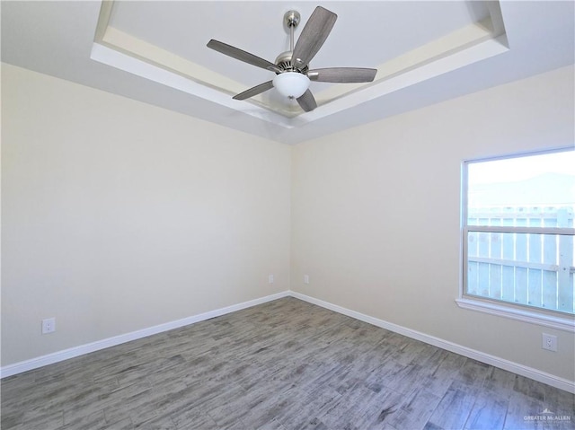 empty room with hardwood / wood-style floors, ceiling fan, and a tray ceiling