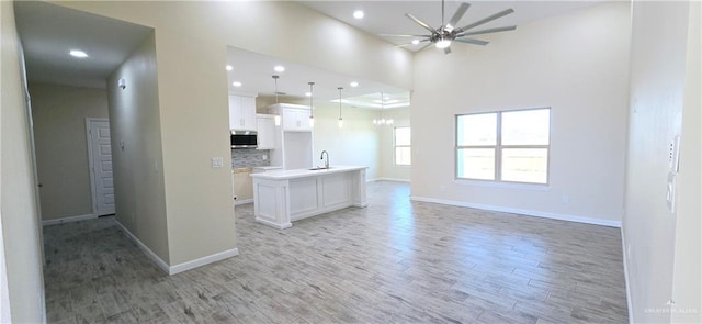 unfurnished living room with a towering ceiling, light hardwood / wood-style floors, ceiling fan, and sink