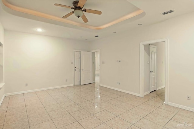 tiled empty room featuring a raised ceiling and ceiling fan