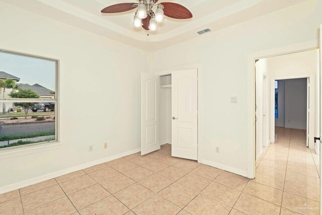 unfurnished bedroom featuring light tile patterned floors, a tray ceiling, and ceiling fan