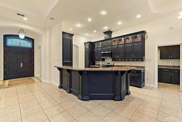 kitchen featuring stone counters, a center island with sink, a breakfast bar area, light tile patterned flooring, and stainless steel appliances