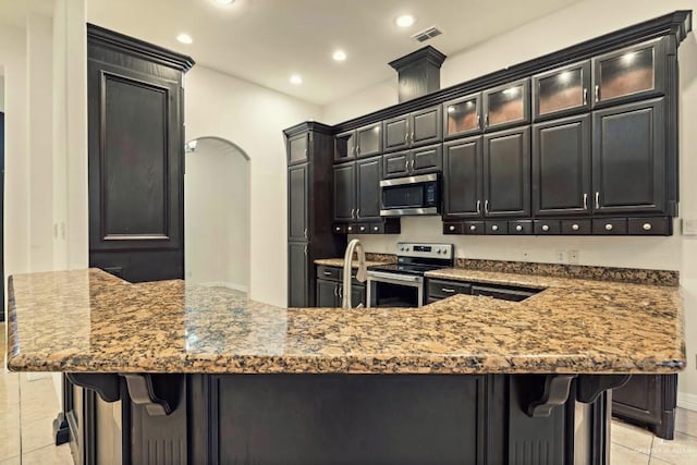 kitchen featuring appliances with stainless steel finishes, light tile patterned floors, a breakfast bar area, and light stone counters