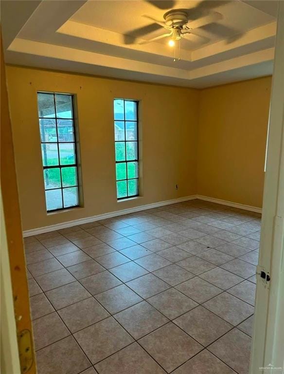 tiled empty room featuring plenty of natural light, ceiling fan, and a tray ceiling