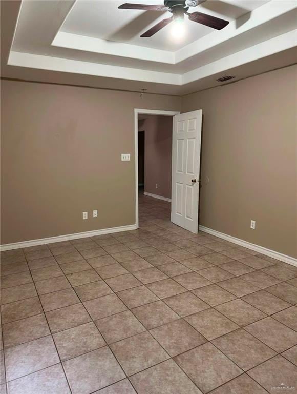 tiled empty room with a tray ceiling and ceiling fan