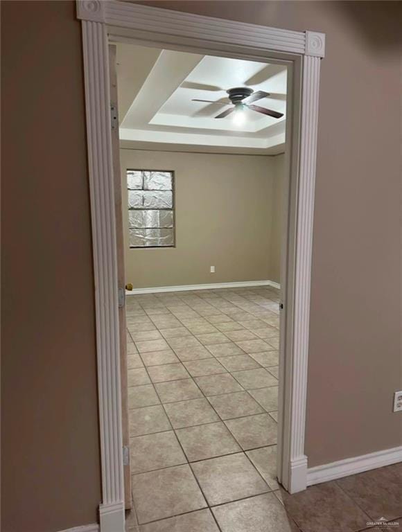 tiled spare room featuring a raised ceiling and ceiling fan