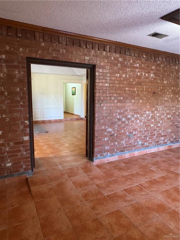 tiled empty room with ornamental molding, brick wall, and a textured ceiling