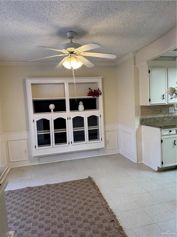 unfurnished dining area featuring ornamental molding, light tile patterned floors, a textured ceiling, and ceiling fan