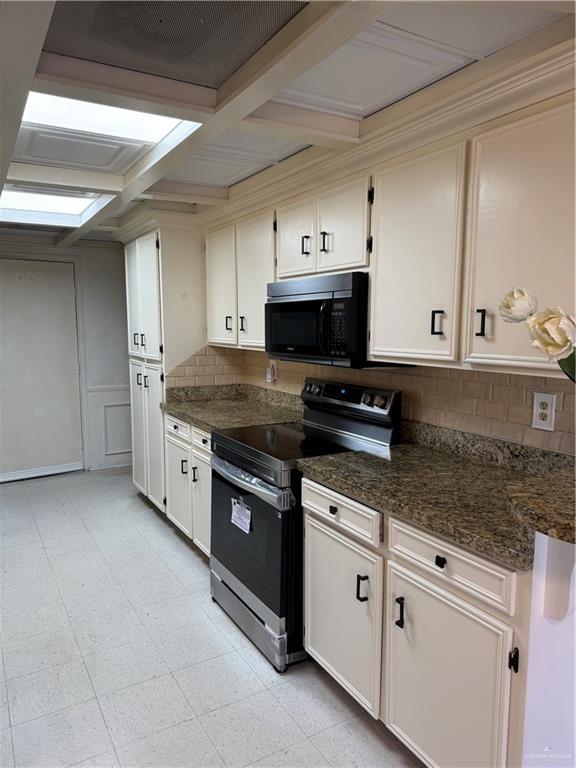 kitchen with white cabinets, coffered ceiling, electric range, and dark stone counters