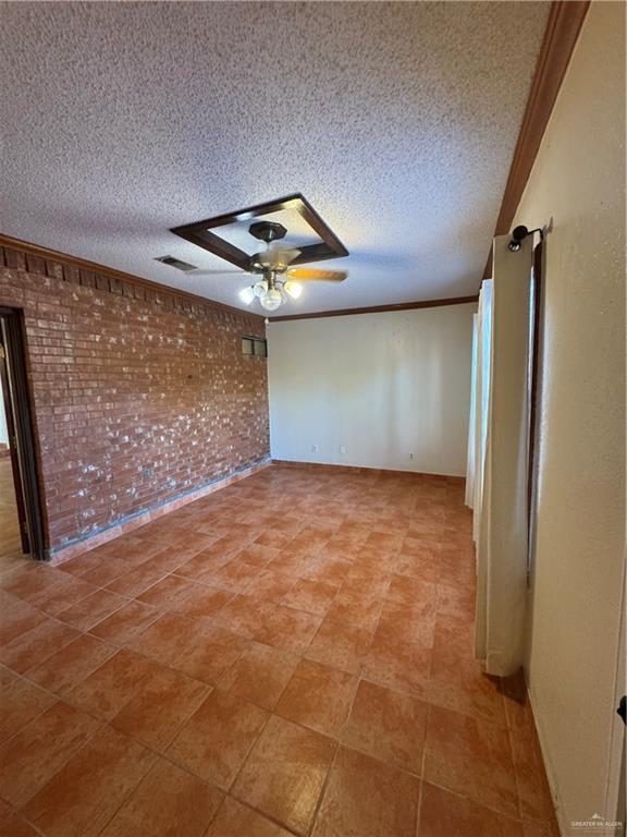 unfurnished room featuring ceiling fan, crown molding, a textured ceiling, and brick wall