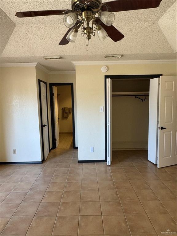 unfurnished bedroom with light tile patterned floors, crown molding, ceiling fan, a textured ceiling, and a closet