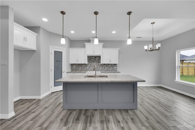 kitchen featuring an island with sink, white cabinetry, a sink, and decorative light fixtures