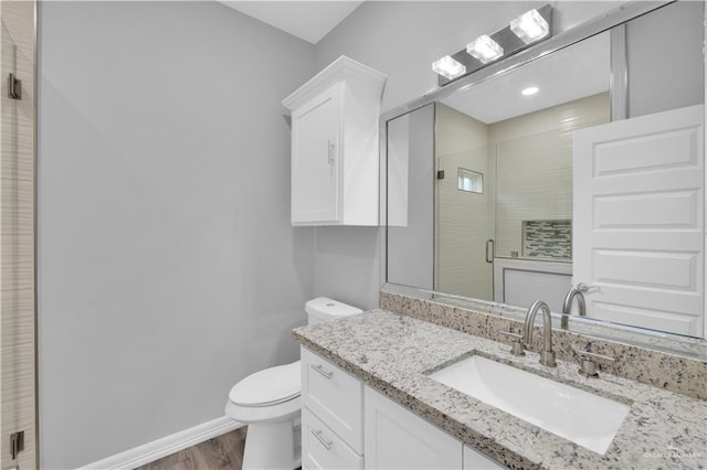 bathroom with toilet, wood finished floors, vanity, baseboards, and a stall shower