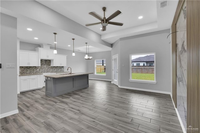 kitchen with tasteful backsplash, white cabinets, an island with sink, open floor plan, and hanging light fixtures