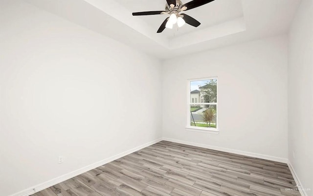 unfurnished room featuring a raised ceiling, ceiling fan, and light hardwood / wood-style flooring