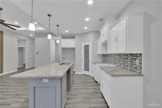 kitchen with light stone counters, decorative light fixtures, white cabinets, a kitchen island with sink, and a sink