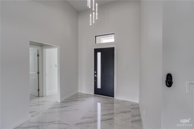 foyer featuring baseboards, marble finish floor, and a towering ceiling