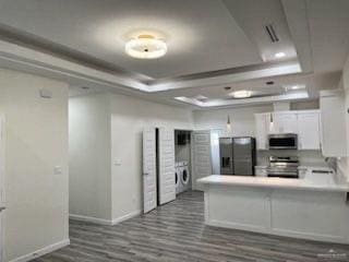 kitchen featuring a raised ceiling, kitchen peninsula, washer / dryer, white cabinets, and appliances with stainless steel finishes