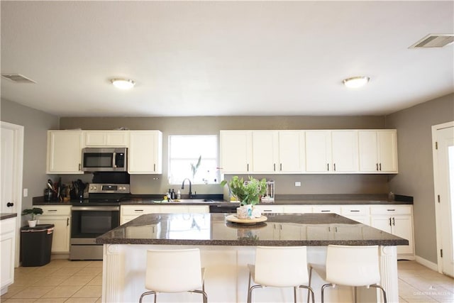 kitchen with stainless steel appliances, a sink, white cabinets, a center island, and a kitchen bar