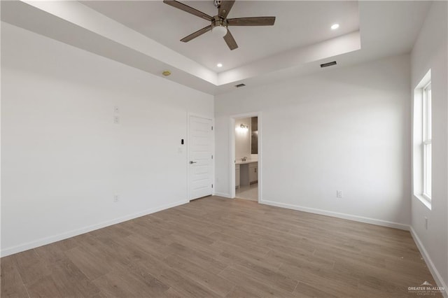 spare room featuring a tray ceiling, a ceiling fan, light wood-type flooring, baseboards, and recessed lighting