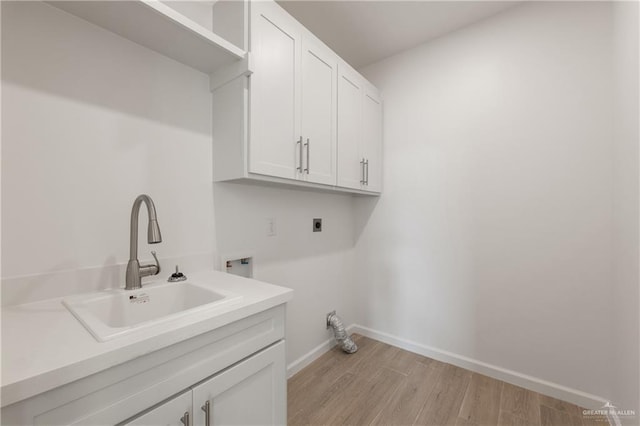 washroom featuring baseboards, a sink, light wood-style floors, hookup for an electric dryer, and cabinet space