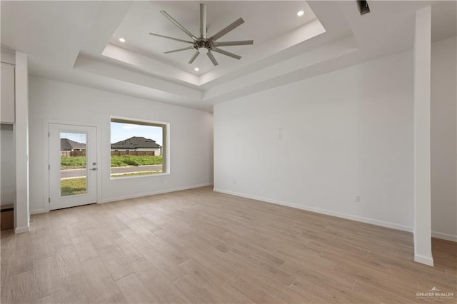 spare room featuring a tray ceiling, baseboards, light wood-style floors, and ceiling fan