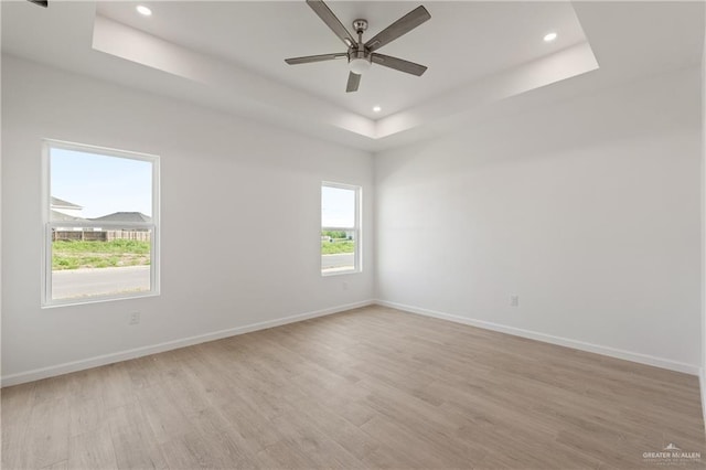 spare room featuring a raised ceiling, light wood-type flooring, baseboards, ceiling fan, and recessed lighting