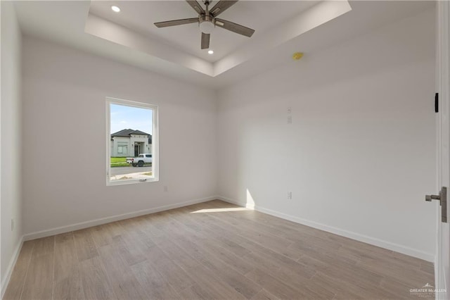 spare room with baseboards, recessed lighting, a ceiling fan, a raised ceiling, and light wood-style floors
