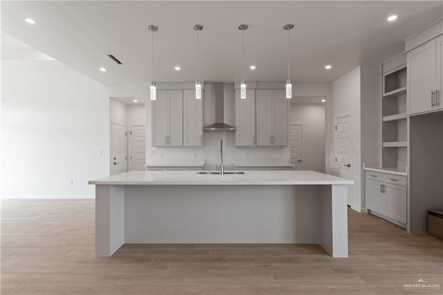 kitchen featuring visible vents, wall chimney exhaust hood, a sink, light wood-type flooring, and a large island with sink